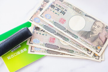 テーブルの上に置かれた銀行の預金通帳と印鑑、1万円札
