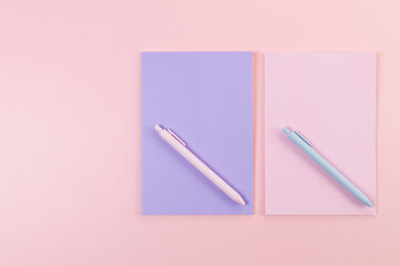 Top view of pink and purple notebooks on pink background. Pink and blue pens, school, office wallpaper. Flat lay, copy space.