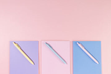 Top view of pink, purple and blue notebooks on pink background. Pink, yellow and blue pens, school, office wallpaper. Flat lay, copy space.