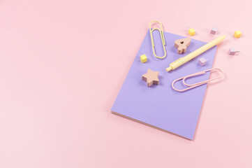 Top view of purple notebook on pink background. Paperclips, pen, number, shape and pins. School, office wallpaper. Flat lay, copy space.