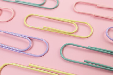 Top view of colorful paperclips on pink background. School, office wallpaper. Flat lay, copy space.