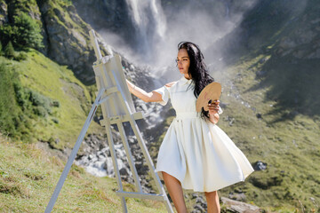 Naklejka premium Artist painting an nature landscape. Beauty woman drawing outdoor. Woman artist draw pictures in waterfall. Female artist paints a picture on canvas. Painting Outdoors. Girl with Canvas Brushes.