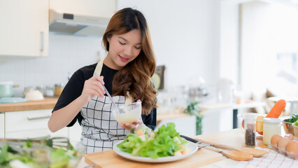 Young asian woman use spoon to adding mayonnaise into salad on plate while preparing fresh...