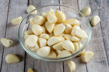 high angle shot of a glass bowl of garlic with scattered garlic on wooden table