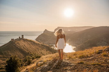 Fototapeta premium A woman stands on a hill overlooking a body of water. The sky is clear and the sun is shining brightly. The woman is enjoying the view and the peaceful atmosphere.