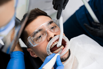 Dentist removes plaque from teeth with airflow equipment. Dental hygiene procedure. Airflow teeth...
