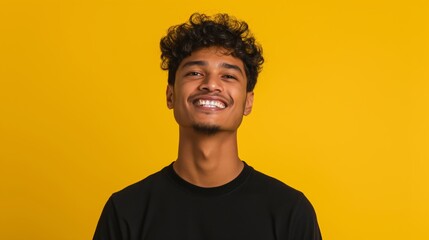 Obraz premium A man with a black shirt and curly hair is smiling at the camera. The image has a bright and cheerful mood, as the man's smile and the yellow background create a positive atmosphere