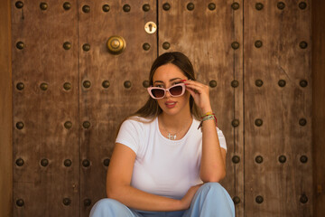 Beautiful young woman with brown hair, sunglasses, white t-shirt and blue pants, looking over the...