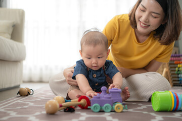 Fototapeta premium A tiny child cheerfully plays with toys on the floor of the living room with mom