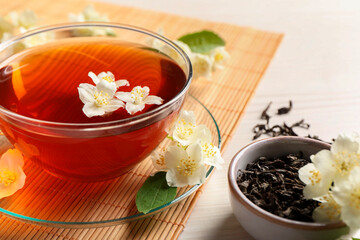 Hot jasmine tea in cup and flowers on white wooden table, closeup
