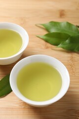 Refreshing green tea in cups and leaves on wooden table, closeup
