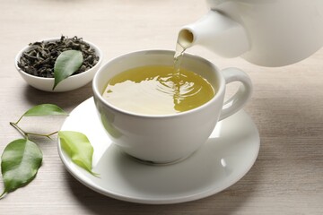 Pouring refreshing green tea into cup at wooden table, closeup