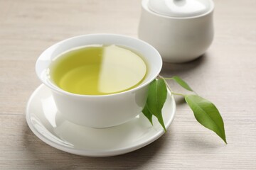 Refreshing green tea in cup, sugar bowl and leaves on wooden table, closeup