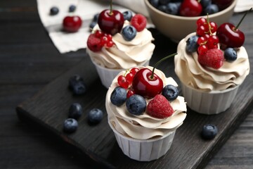 Tasty cupcakes with different berries on black wooden table, closeup