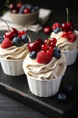 Tasty cupcakes with different berries on black wooden table, closeup