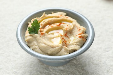 Delicious hummus with olive oil, parsley and paprika in bowl on white textured table, closeup