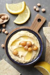 Delicious hummus with olive oil, chickpeas, lemon and pita on grey textured table, flat lay