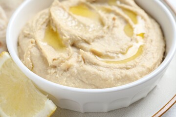 Delicious hummus with olive oil in bowl and lemon on white table, closeup