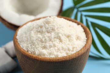 Fresh coconut flour in bowl, nut and palm leaf on light blue table, closeup