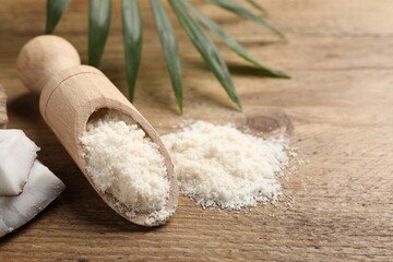 Coconut flour in scoop and leaf on wooden table, closeup. Space for text