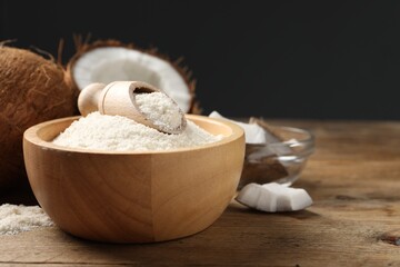 Coconut flour in bowl, scoop and fresh fruits on wooden table, closeup. Space for text