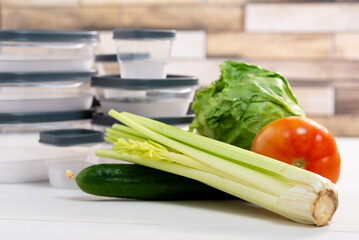 A stack of plastic containers and raw vegetables on the table. Storage for vegetables and fruits in plastic containers