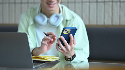 Smiling young man using mobile phone at cafe table, typing message or chatting on social media app