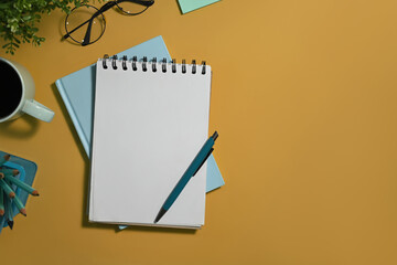 Spiral notepad, pen, eyeglasses and cup of coffee on yellow background with copy space