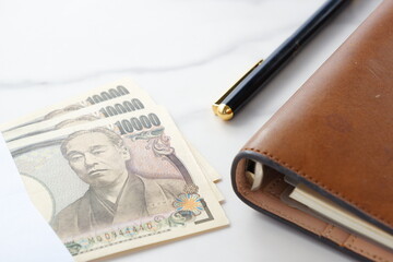 福沢諭吉の肖像の一万円紙幣と、茶色の革の手帳
