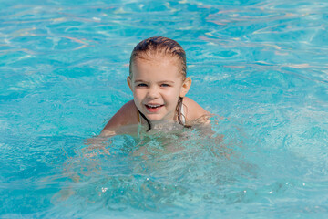 A girl happily splashes around in the pool, enjoying a summer day. Perfect for advertising related to children's activities, family events, and summer products.