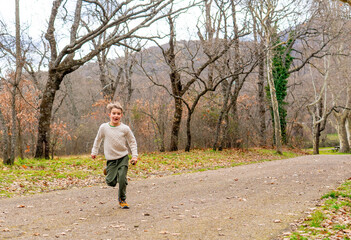 Obraz premium Caucasian boy running with funny face looking at camera in a park in autumn