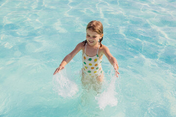 A girl happily splashes around in the pool, enjoying a summer day. Perfect for advertising related to children's activities, family events, and summer products.