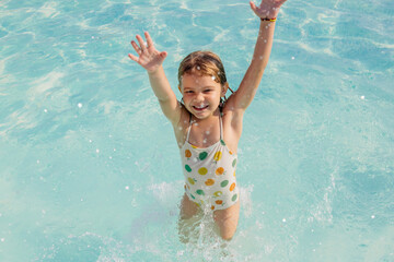 A girl happily splashes around in the pool, enjoying a summer day. Perfect for advertising related to children's activities, family events, and summer products.