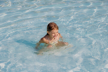 A little girl plays happily in the pool, splashing in the crystal-clear water. A joyful moment of freedom on a sunny day.