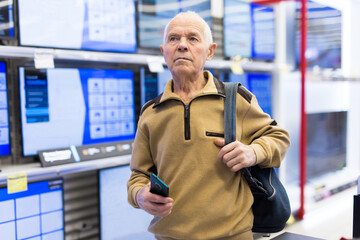 Elderly grayhaired man pensioner looking counter with modern digital televisors in showroom of digital goods store