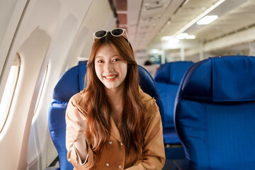 An Asian woman travels abroad by plane, sitting near the window. She listens to music while flying, looks at her phone, uses a tablet, and smiles happily, enjoying her trip.