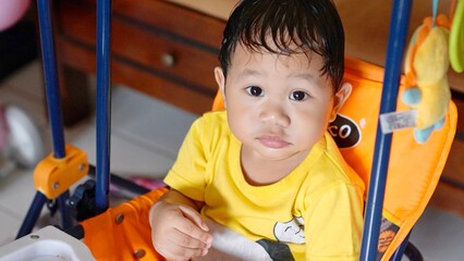 A young boy is sitting in a high chair with a yellow shirt on