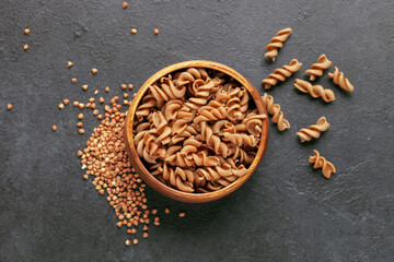 Wholegrain pasta in bowl and buckwheat on dark background. Top view