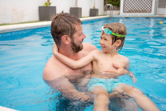 Portrait of caucasian father swimming in pool with little son.