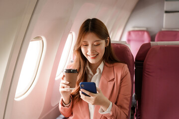 An Asian businesswoman takes a plane ride near the window to travel for a business discussion. She smiles while looking out the window, enjoying the journey and preparing for her meetings.