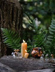witch cauldron, candles and qurtz crystals on stump in forest, abstract natural background. occult...