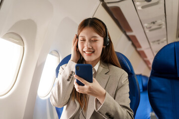 An Asian businesswoman travels abroad by plane, sitting near the window. She reads a book and uses her computer, utilizing her airline credit card to manage travel expenses efficiently.