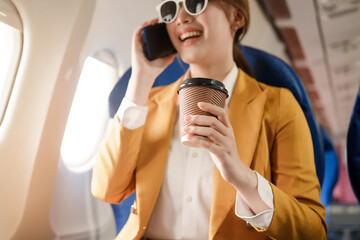 Naklejka premium An Asian businesswoman travels abroad by plane, sitting near the window. She reads a book and uses her computer, utilizing her airline credit card to manage travel expenses efficiently.