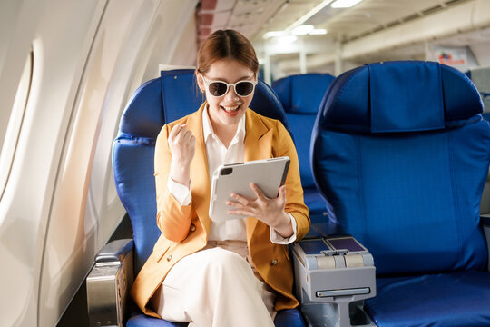 An Asian businesswoman travels abroad by plane, sitting near the window. She reads a book and uses her computer, utilizing her airline credit card to manage travel expenses efficiently. - Powered by Adobe