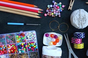 Colorful beads, coloring pencils, glitter, needles, string, hoop, tape and scissors on dark...