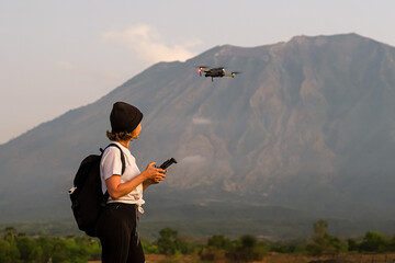 A girl of European appearance, a traveler with a backpack, shoots a video with a drone, against the backdrop of beautiful mountains.