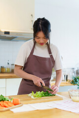 Asian women chopping slices lettuce with knife on cutting board to preparing fresh vegetables of...