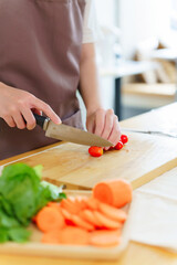 Asian women chopping slices tomatoes with knife on cutting board to preparing fresh vegetables of ingredients for cooking breakfast meal while making healthy food lifestyle in the kitchen at home