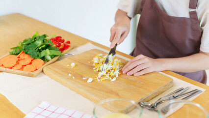 Closeup hands of asian women chopping boil egg with knife on cutting board and slice fresh vegetable to preparing ingredients for cooking breakfast meal while making healthy food lifestyle in kitchen