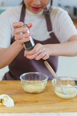 Asian women adding mayonnaise and pepper in chopped boiled eggs to mixing dressing of salad while preparing ingredients for cooking breakfast meal and making healthy food lifestyle in kitchen at home